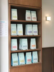Wooden cabinet filled with rows of light blue coffee bag packaging on shelves with a small menu on the left wall
