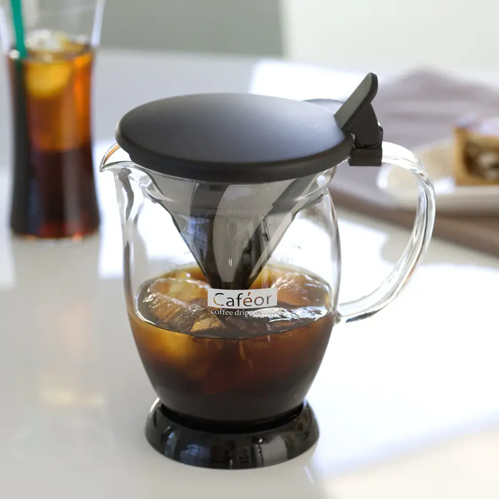 Glass coffee carafe with a black lid and pour over dripper brewing dark coffee on a kitchen counter