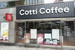 Front of a Cotti Coffee shop with a large white Cotti Coffee sign on a dark panel glass doors and posters in the windows