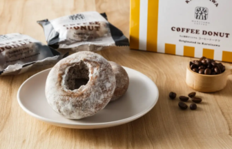 Powdered sugar donuts on a white plate with coffee beans nearby and a yellow and white Coffee Donut box in the background