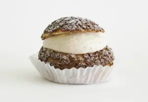 Cream puff sandwich with vanilla bean cream filling dusted with powdered sugar in a white paper liner