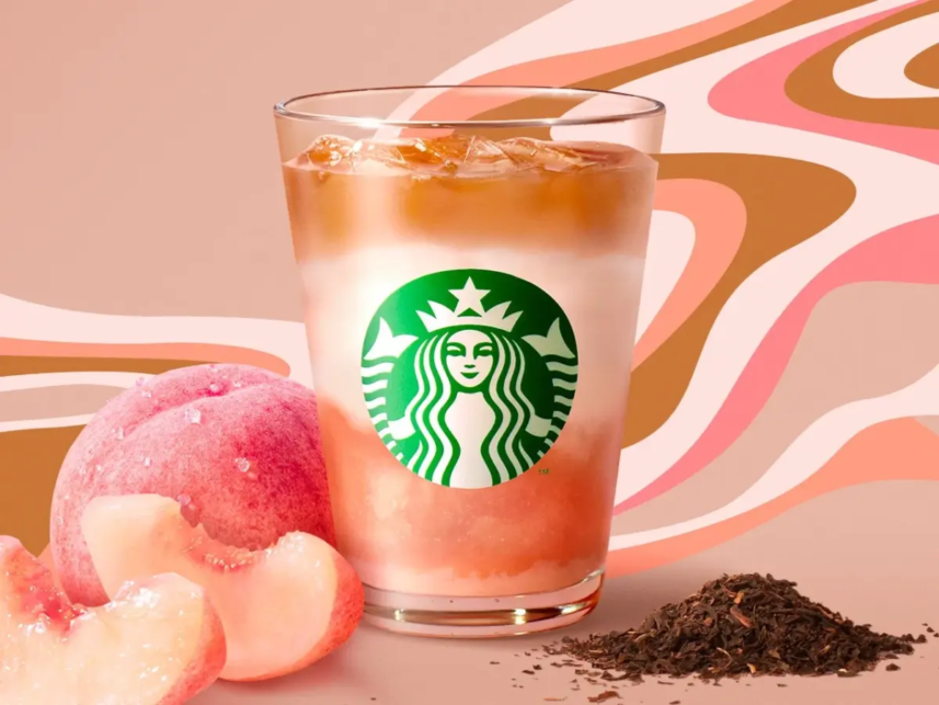 Starbucks iced peach flavored drink in a glass with peaches and loose tea leaves on a pink patterned backdrop