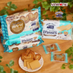 Assorted Sanritsu Dasses cookies in turquoise packaging on a wooden table with a plate of baked treats in the foreground Includes visible product names and wrappers