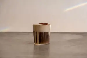 Chocolate mousse parfait in a clear glass with a cream topping and chocolate drizzle on a gray counter surface