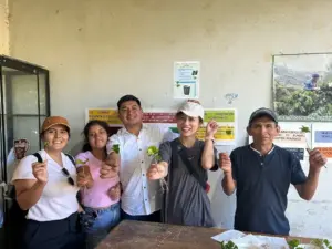 Group of five people proudly holding young plant seedlings for a garden or class activity at a community site