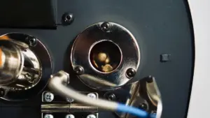 Close up of metallic mechanical components circular chrome plates screws and a central hollow cylinder with visible inner parts blue wire in foreground
