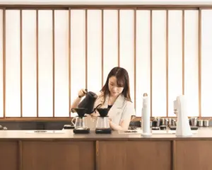 Barista pours hot water over glass pour over cones at a wooden counter in a cafe setting