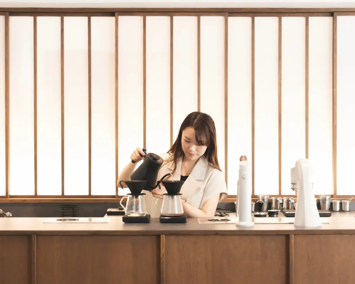 和風の落ち着いたカフェで、女性がハンドドリップコーヒーを淹れている様子
