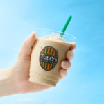 Hand holding a cold iced coffee cup from Tullys Coffee with a green straw against a blue background