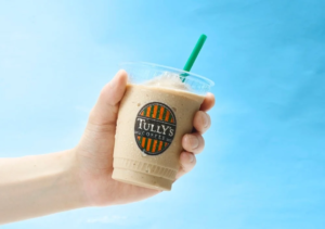 Hand holding a cold iced coffee cup from Tullys Coffee with a green straw against a blue background