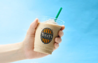 Hand holding a cold iced coffee cup from Tullys Coffee with a green straw against a blue background