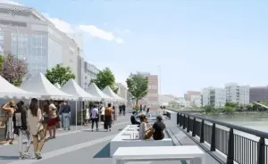 Outdoor riverside market with white tents and people browsing stalls along a boardwalk