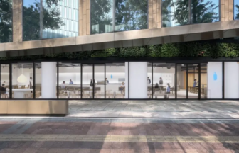Modern glass front cafe with interior seating and customers set in a urban plaza with a bench and greenery outside