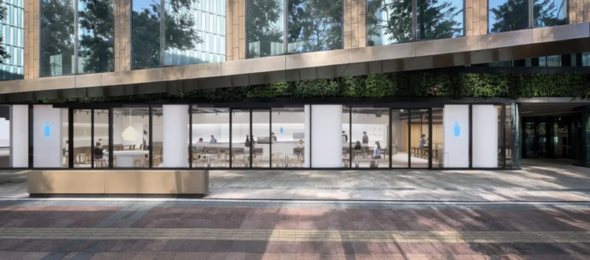 Modern glass front cafe with interior seating and customers set in a urban plaza with a bench and greenery outside