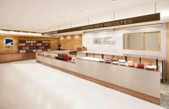 Modern bakery counter with cakes on display and product shelves sign reading SAISON DES RECOLTES on the back wall in a bright shop interior