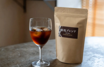 Glass of iced coffee in a stemmed glass beside a kraft coffee bag labeled Original Premium Coffee on a kitchen counter