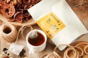 White tea pouch with a yellow label beside a cup of tea on a wooden table