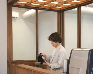 Person in a light blazer pouring water over a pour over coffee setup at a wooden counter in a cafe area