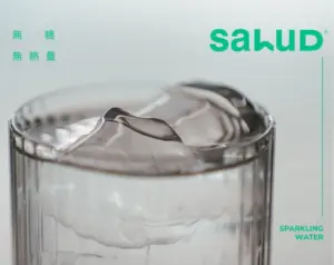 Glass filled with ice and clear sparkling water Salud logo in teal on the right with SPARKLING WATER text nearby in teal and small teal characters on the left edge
