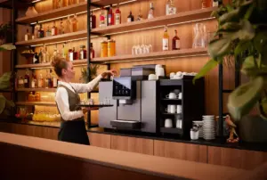 Barista preparing coffee with an espresso machine behind a bottle filled bar setting in warm light