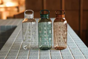 Three patterned glass water bottles with loop caps on a tiled counter left to right clear teal and amber