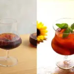Two cocktails side by side in stemmed glasses on wooden surfaces left is dark right is red with mint garnish and a sunflower in the background