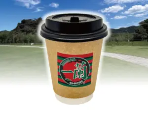 Disposable coffee cup with black lid and Ichiran logo outdoors in a park