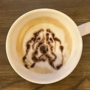 Top down view of a white mug with cappuccino or latte foam swirling with chocolate drizzle in an abstract pattern on a wooden table