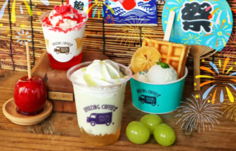 Bright dessert spread two milk based drinks in cups with whipped toppings fruit topping and waffles set on a wooden table with colorful festival banners and fireworks illustrations in the background plus green grapes nearby