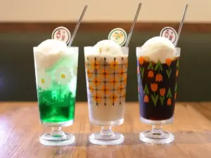 Three tall dessert glasses with vanilla ice cream scoops and colorful decorative prints on a wooden table straws included