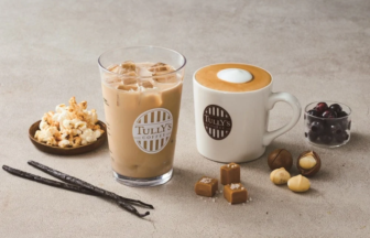 Iced coffee in a glass with ice next to a white mug of latte surrounded by popcorn chocolates vanilla pods and berries on a light surface