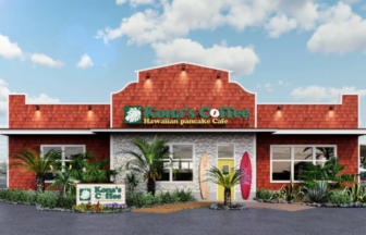Exterior view of Konas Coffee Hawaiian pancake Cafe with a red brick façade tropical plants and surfboards by the entrance