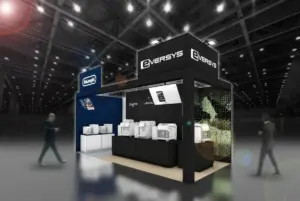 Trade show booth for Eversys with white espresso machines on display under bright hall lights DeLonghi logo visible on a blue wall