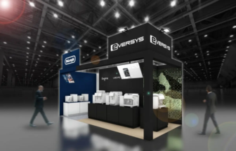 Trade show booth for Eversys with multiple white machines on display and a blue Delonghi sign in a large exhibition hall.