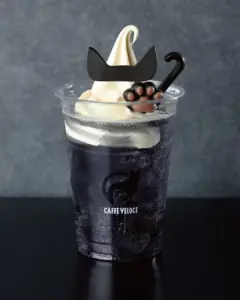 Clear plastic cup of dark soda topped with whipped cream adorned with a black cat paw and mustache decoration and the Caffe Veloce logo