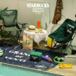 Poolside Starbucks Stand by BEAMS setup with two camping chairs a lace table bag cooler goggles and STARBUCKS STAND logo on the wall