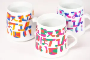 Three white ceramic mugs with bright abstract multicolor patterns covering their surfaces viewed from above and side angles