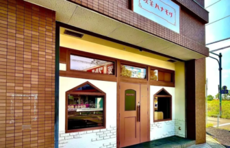 Cafe storefront with a pink door and diamond shaped windows set in a brick facade sign above in Japanese 2 windows flank the door under a white brick wall detail