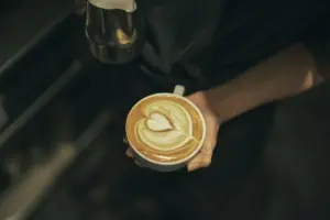Barista holding a cup of latte with a heart shaped latte art on top in a dim cafe setting