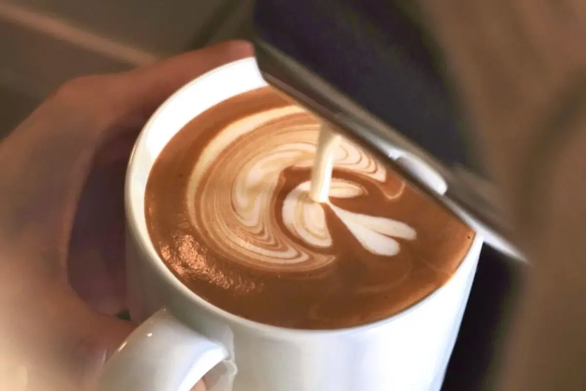 白いマグカップに入ったカフェラテに、ミルクが注がれて美しいハート型のラテアートが作られている瞬間