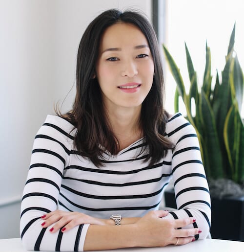 animalprof | コーヒーステーション Woman with dark hair in a white and black striped shirt sits at a table in a bright office