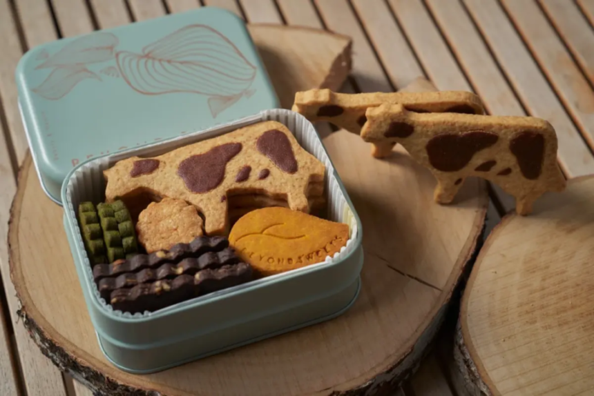 Open light blue tin filled with assorted cookies cow pattern biscuits green wafers chocolate bars on a wooden surface