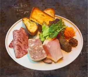 Charcuterie plate with sliced cured meats terrine salad greens crostini and a carrot garnish on a white plate