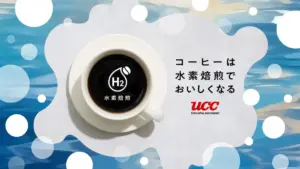 Top down view of a cup of black coffee on a white saucer with a hydrogen H2 logo and Japanese text beside plus the UCC branding in the background