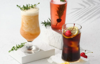 Three colorful cocktails on white blocks with lemon slice and cherries as garnishes