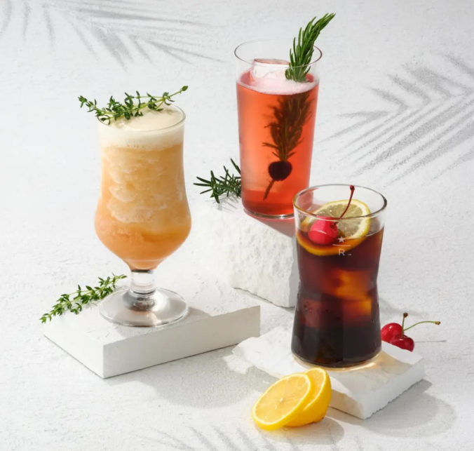 Three colorful cocktails on white blocks with lemon slice and cherries as garnishes