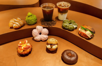 Assorted donuts and pastries arranged on curved brown steps with two coffee drinks in the background, cafe display.