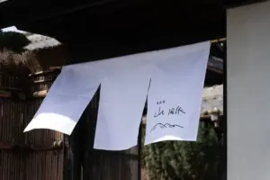 White fabric signage noren with Japanese calligraphy and a simple mountain drawing hanging outside a traditional building