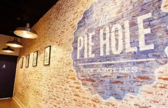 Brick walled hallway with industrial pendant lights and framed pictures on the left a large blue mural with the text the HOLE on the right wall