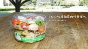 Takeout salad cup on a wooden table outdoors Japanese text promotes 100 plant based substitutes
